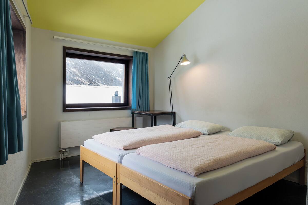 A bedroom with two beds, a window with curtains, a desk, and a lamp.