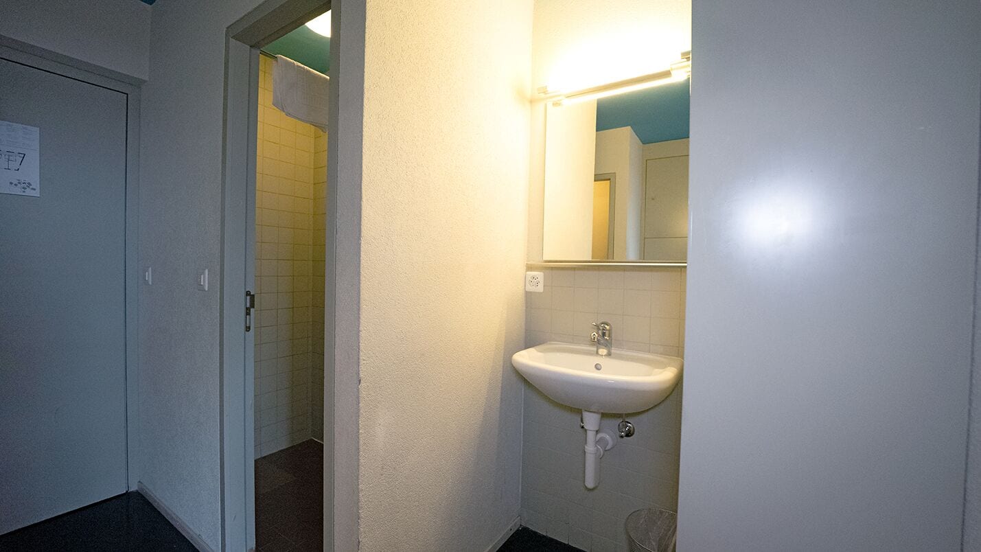 Ein Badezimmer mit einem weißen Waschbecken, einem Spiegel und einer Tür zu einem Duschbereich.