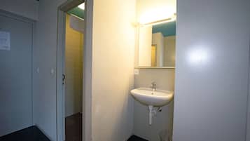 Ein Badezimmer mit einem weißen Waschbecken, einem Spiegel und einer Tür zu einem Duschbereich.