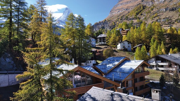 Un refugio de montaña con varias cabañas de madera, un telesilla y montañas nevadas al fondo.