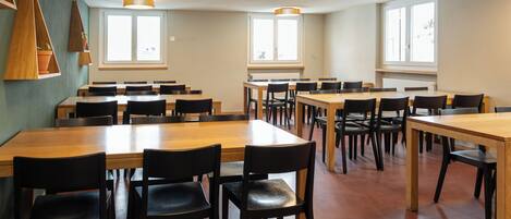 A spacious dining area with multiple tables and chairs, large windows providing natural light, and a modern ceiling design.