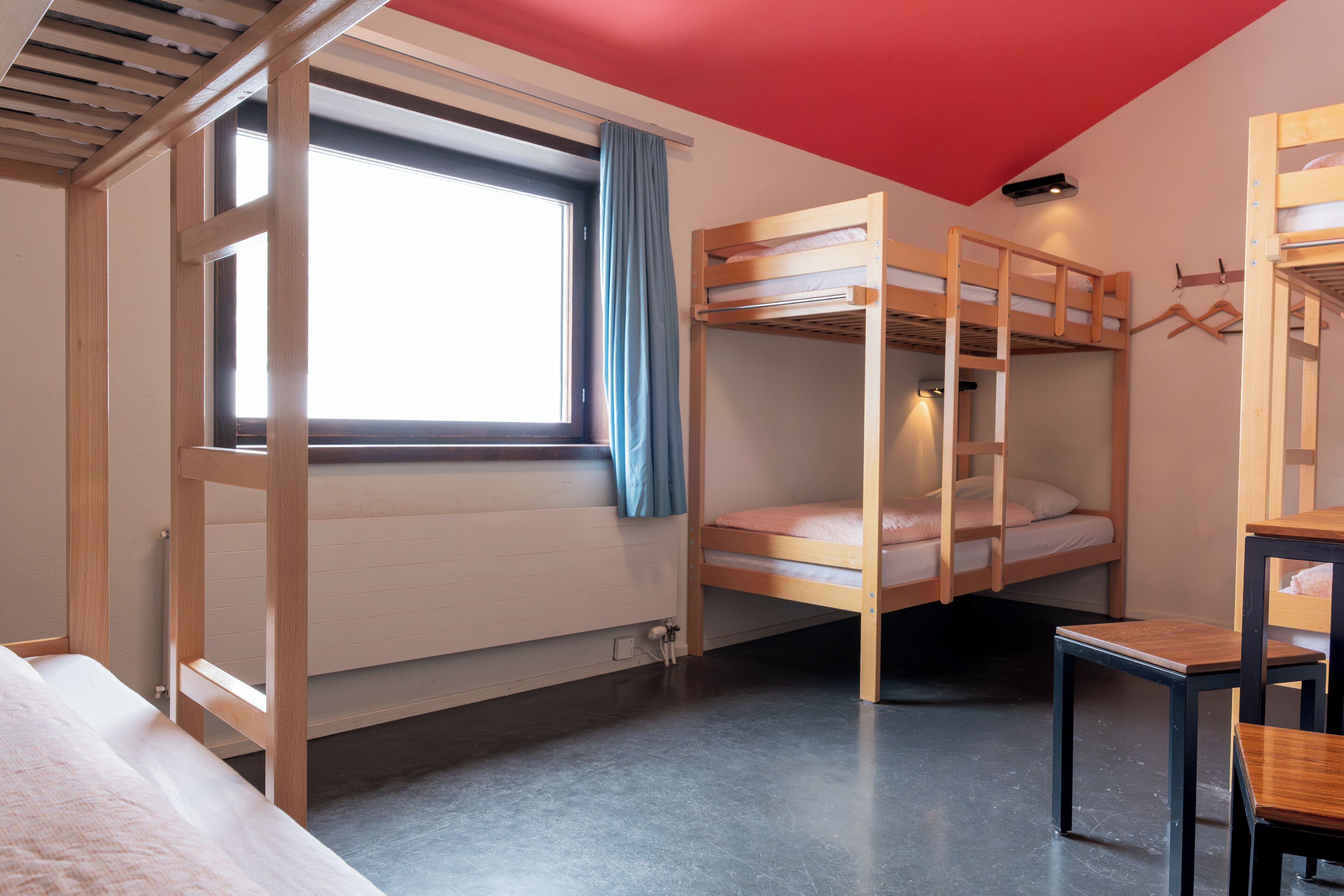 A bunk bed room with a window, a table, and a red ceiling.