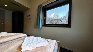 Un dormitorio con cama, ventana y vista de árboles nevados y una montaña.