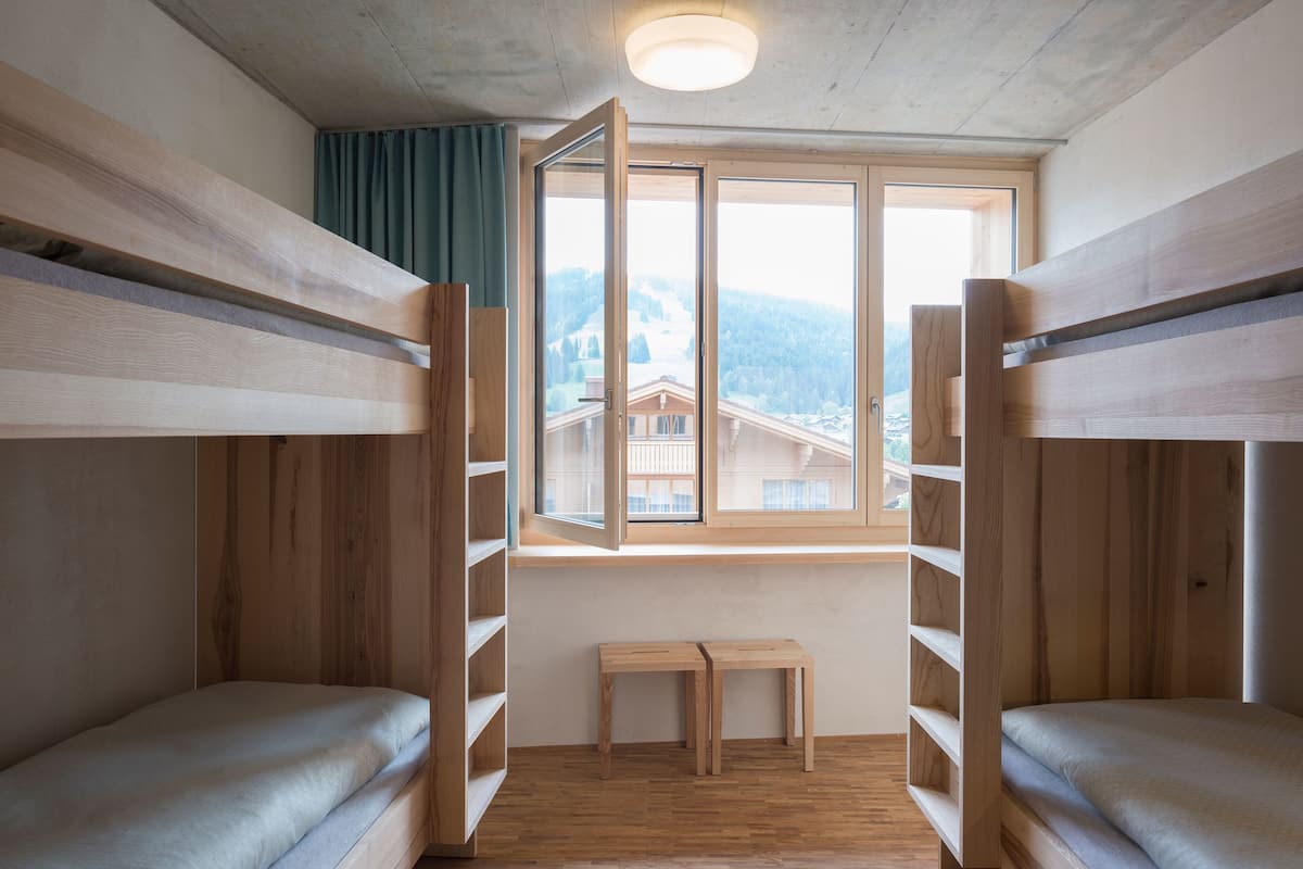 A bunk bed room with a window, wooden walls, and a small bench.