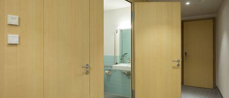 Un couloir avec des portes en bois, une salle de bain avec un lavabo et un miroir, et un sol carrelé.