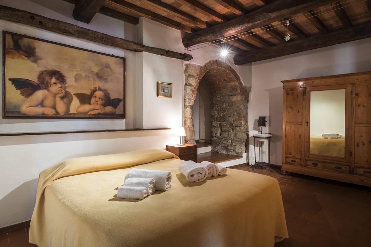 Une pièce comprenant un lit, une arche en pierre, une armoire en bois et un tableau accroché au mur.