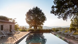 Un área junto a la piscina con sillones de descanso y un edificio de piedra.