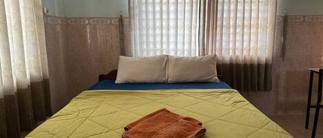 A neatly made bed with a green quilt, a folded brown towel, and two pillows on a blue mattress.
