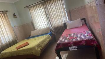 Two single beds with different colored bedspreads, a small table, and a curtain.