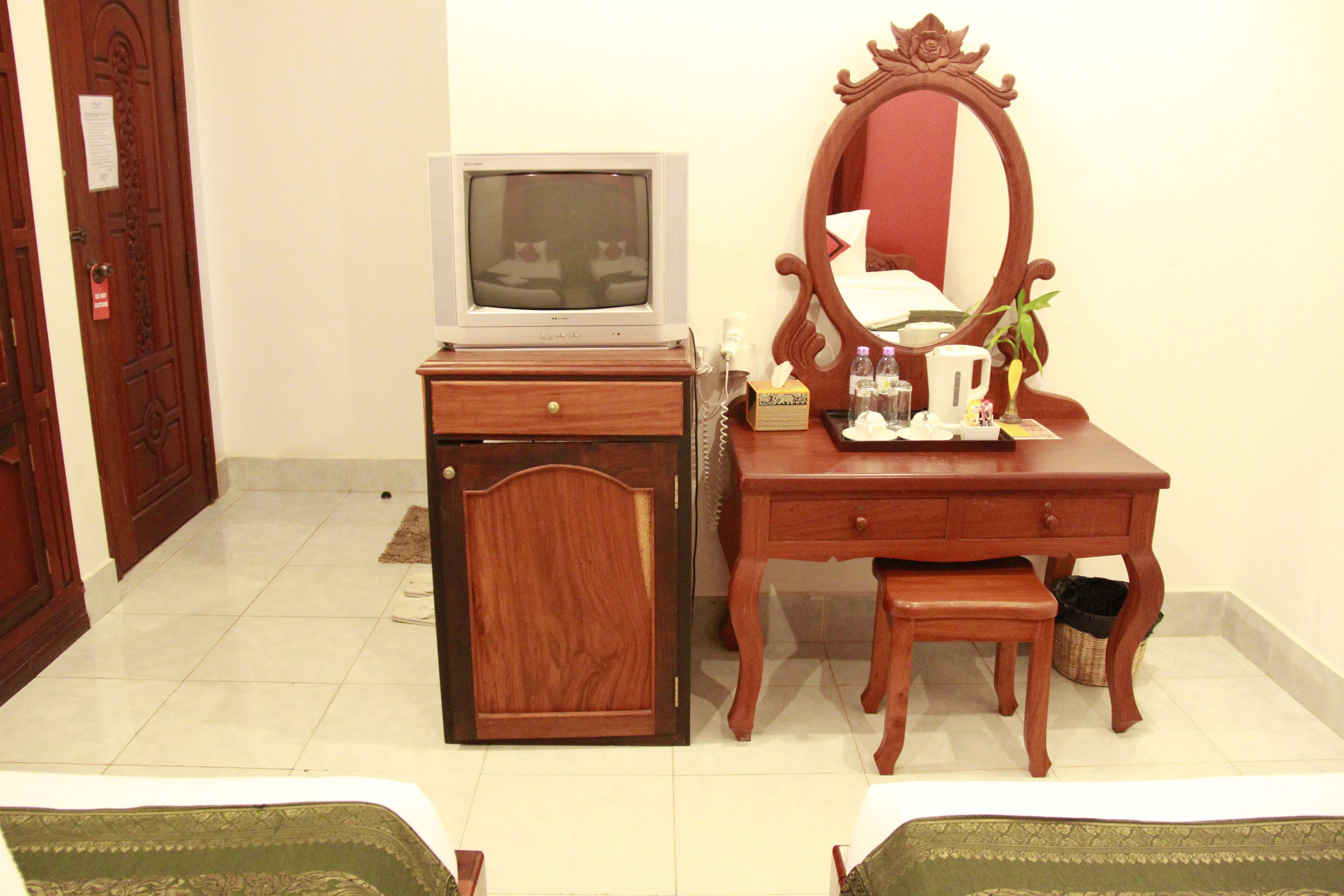 A hotel room with a wooden dresser, a television, a mirror, and a small table with a plant.