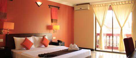 Habitación de hotel con una cama grande, una mesita de noche, una lámpara, aire acondicionado instalado en la pared y vistas al exterior a través de una puerta corrediza de vidrio.