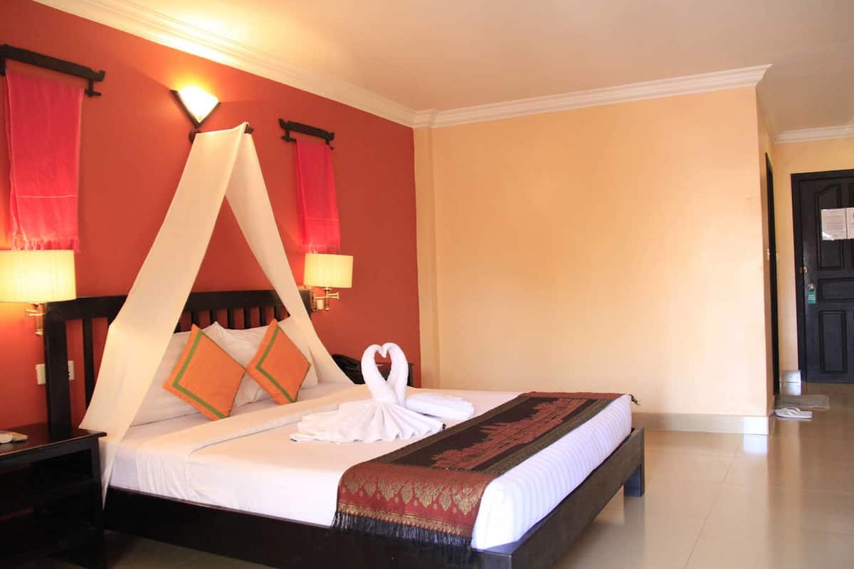 Une chambre d’hôtel avec un lit, une table de chevet, une lampe et une porte.