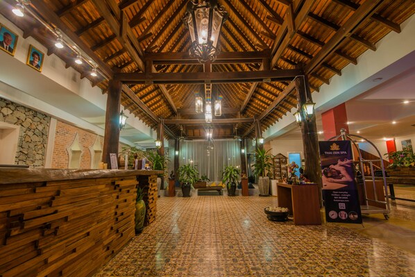 A spacious lobby with a high wooden ceiling, a reception desk, and potted plants.