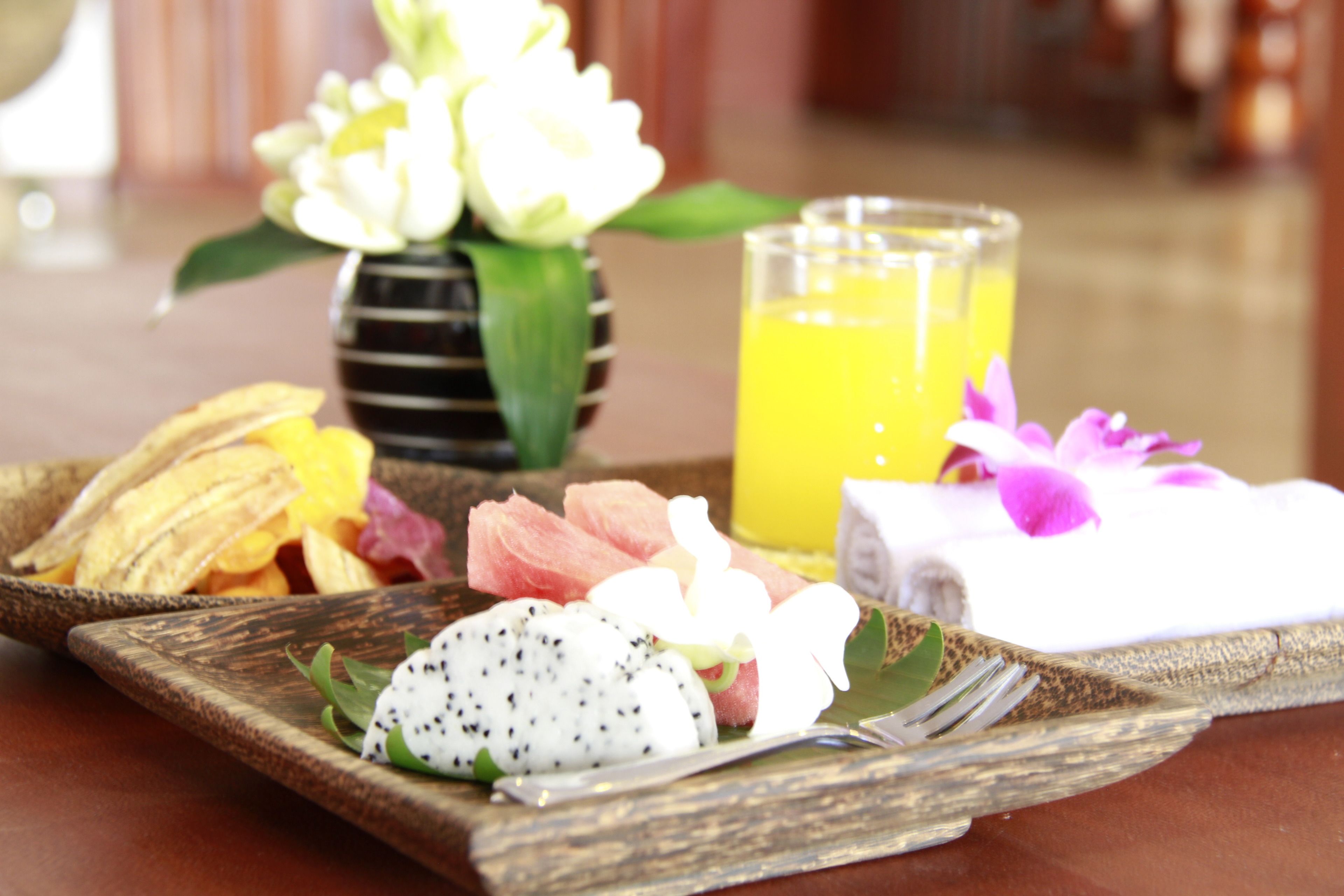 A wooden tray with various fruits, a glass of orange juice, and a small vase with flowers.