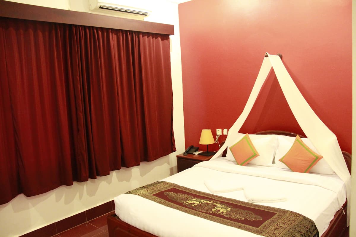 Une chambre d’hôtel avec un lit, des rideaux rouges, une table de chevet avec une lampe et un lit à baldaquin.
