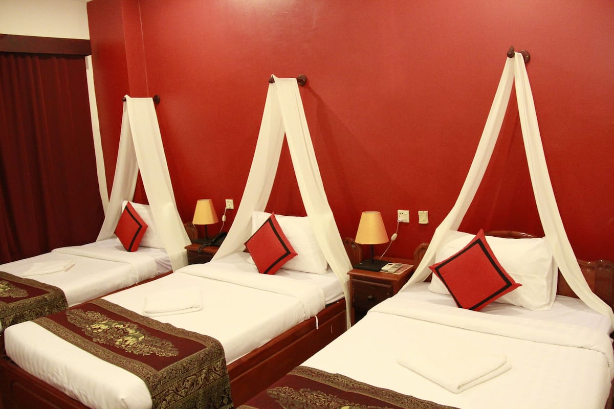 Une chambre d’hôtel avec quatre lits, chacun surmonté d’un dais et agrémenté d’un oreiller rouge.