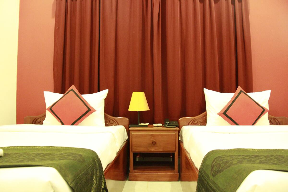 Une chambre d’hôtel avec deux lits, une table de chevet avec une lampe et un rideau en arrière-plan.