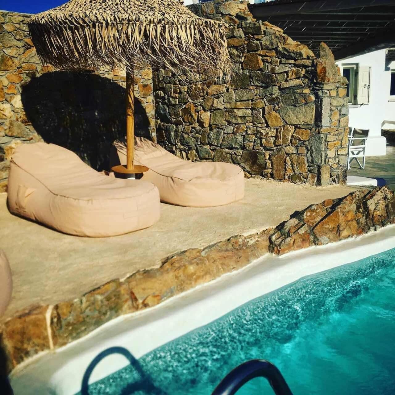 Ein Poolbereich mit Steinmauern und einem Reetdachschirm, mit zwei beigen Sitzsäcken.