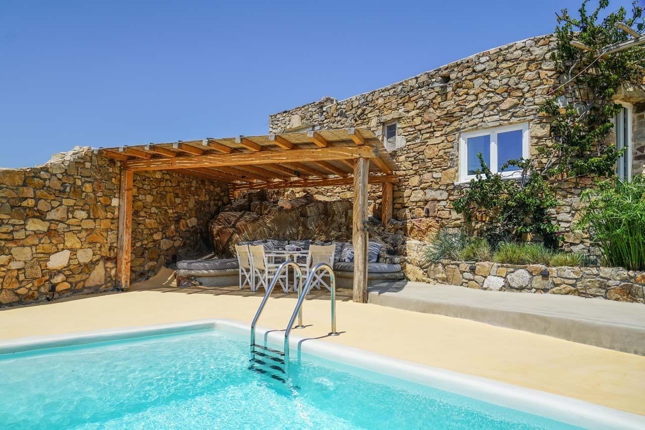 En bygning i sten med swimmingpool, udendørs møbler og et pergola.