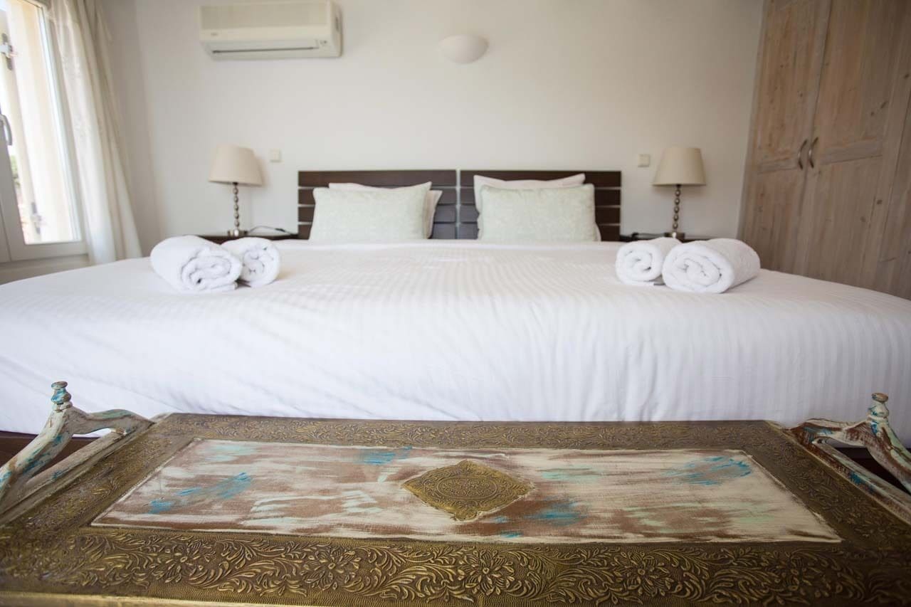 Habitación de hotel con una cama grande, dos lámparas de noche, un armario de madera y una mesa decorada con un mantel estampado.