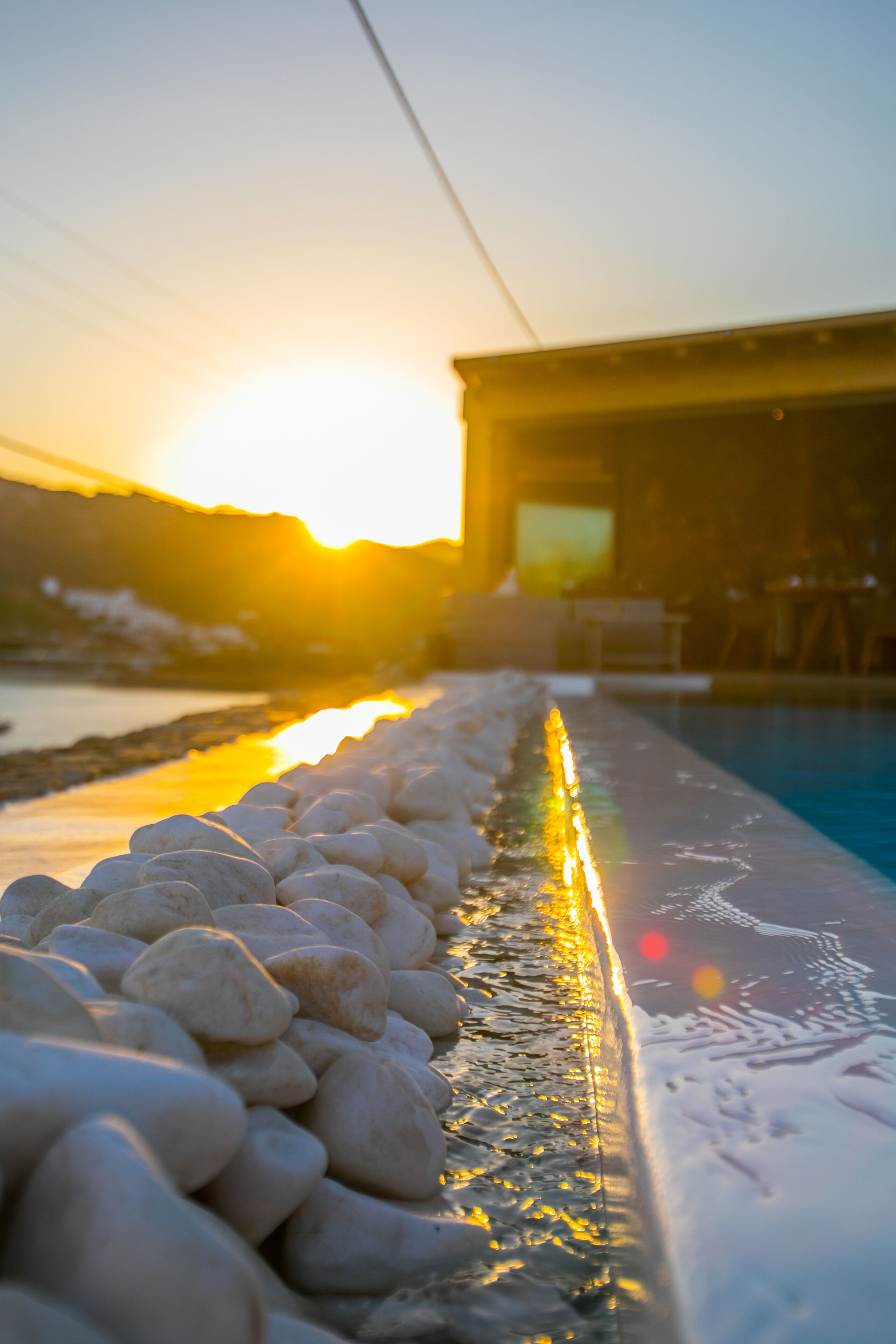 A poolside area with a row of white pebbles and a reflection of the sunset.