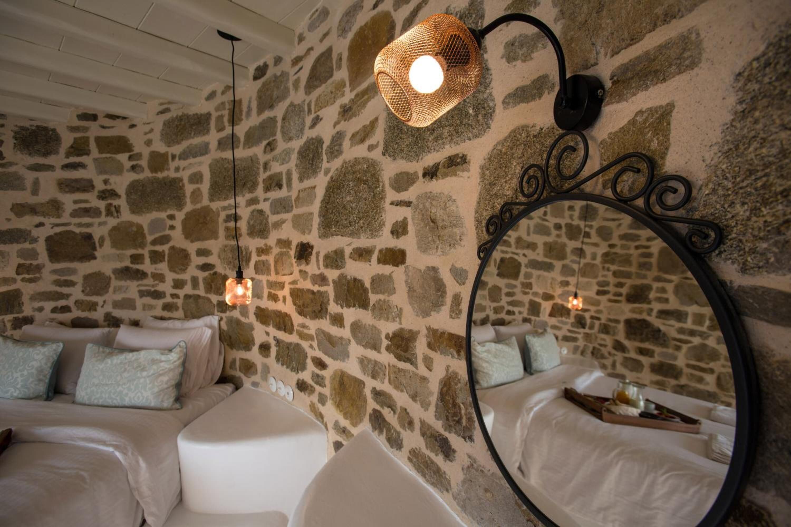 A cozy room with a stone wall, a round mirror, and a bed with white bedding and blue pillows.