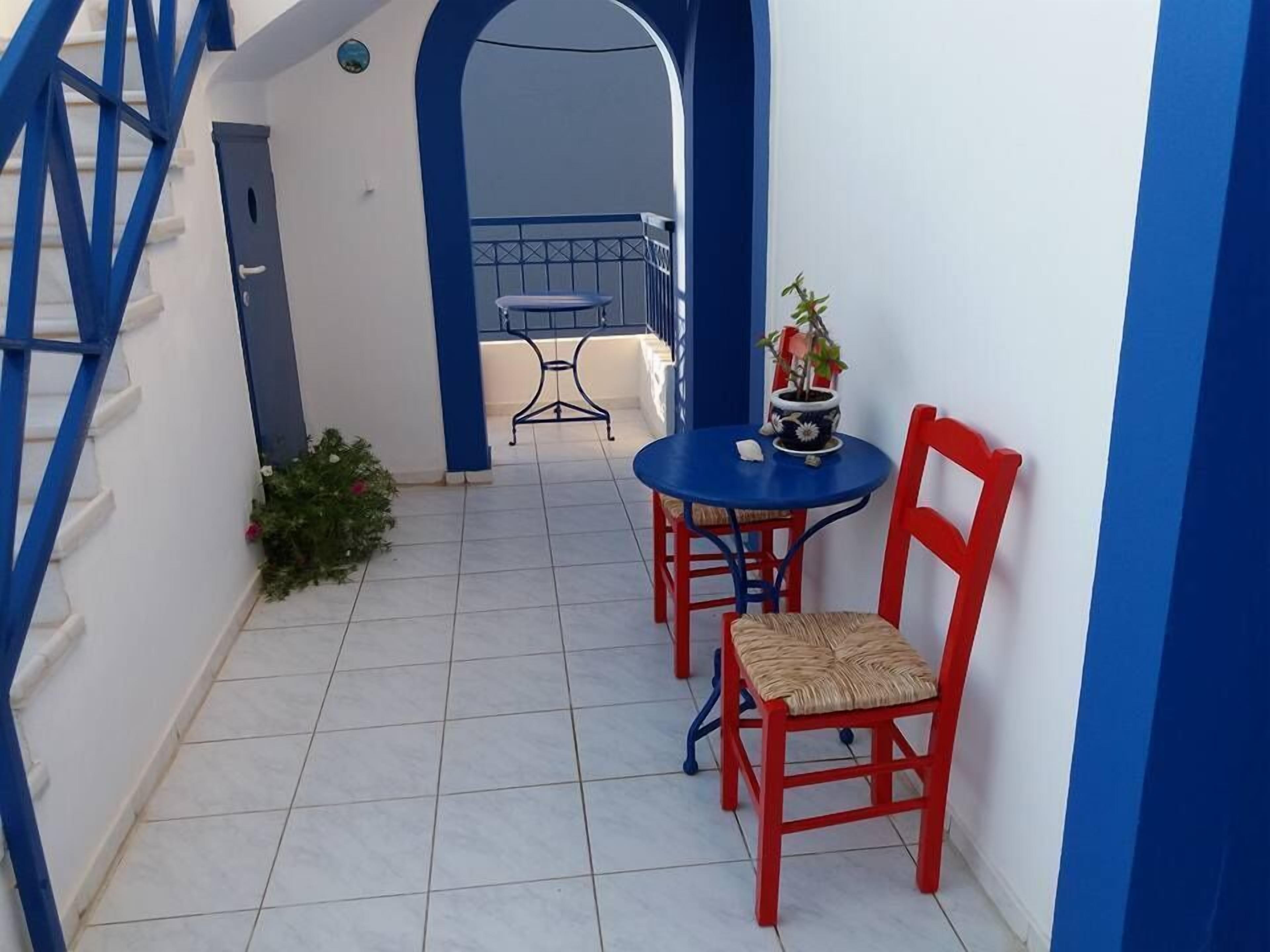Un piccolo patio esterno con un tavolo blu e sedie rosse, una pianta in vaso e vista su un balcone.