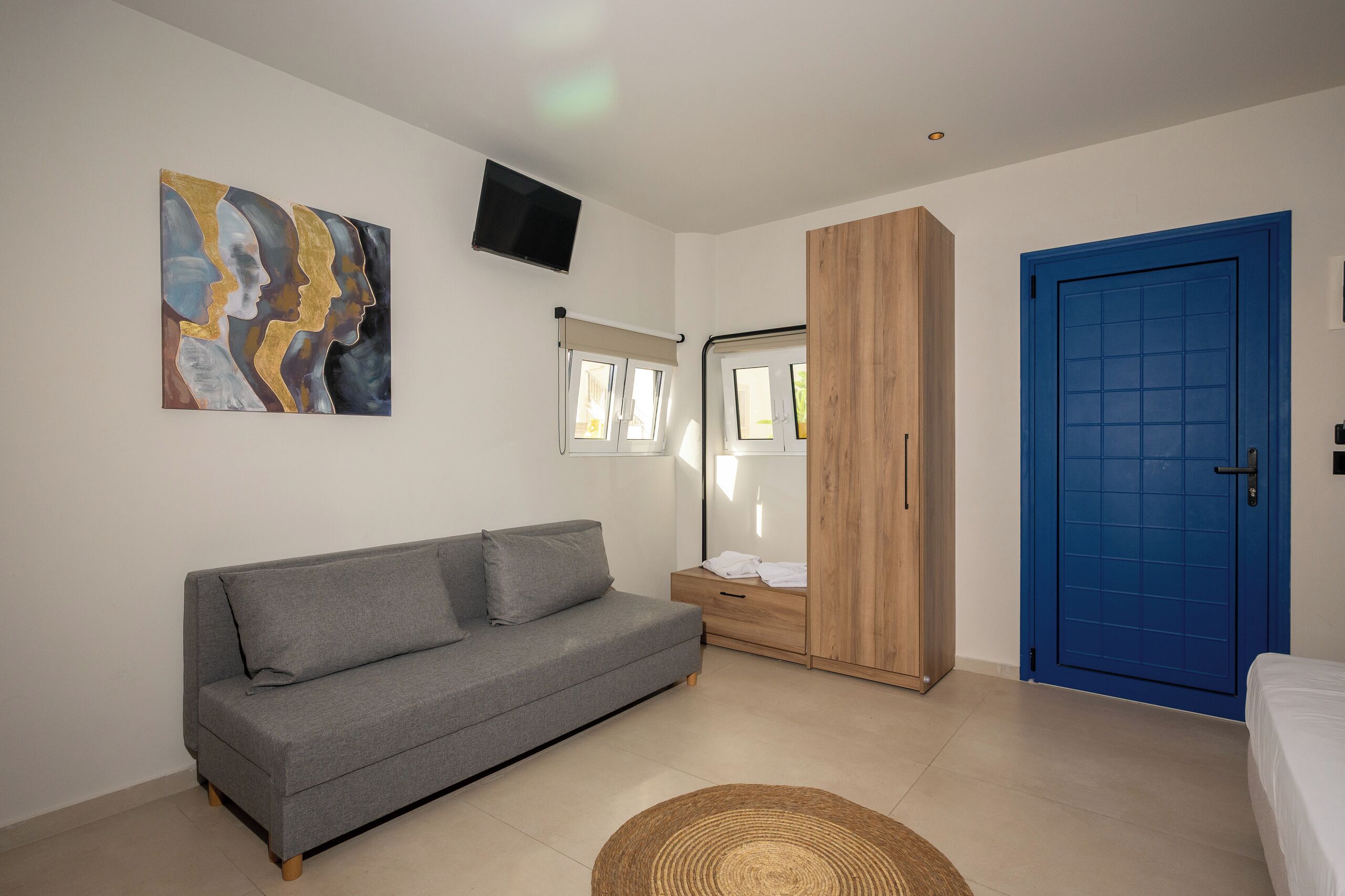 A modern room with a grey sofa, a wooden wardrobe, a blue door, and a wall-mounted TV.