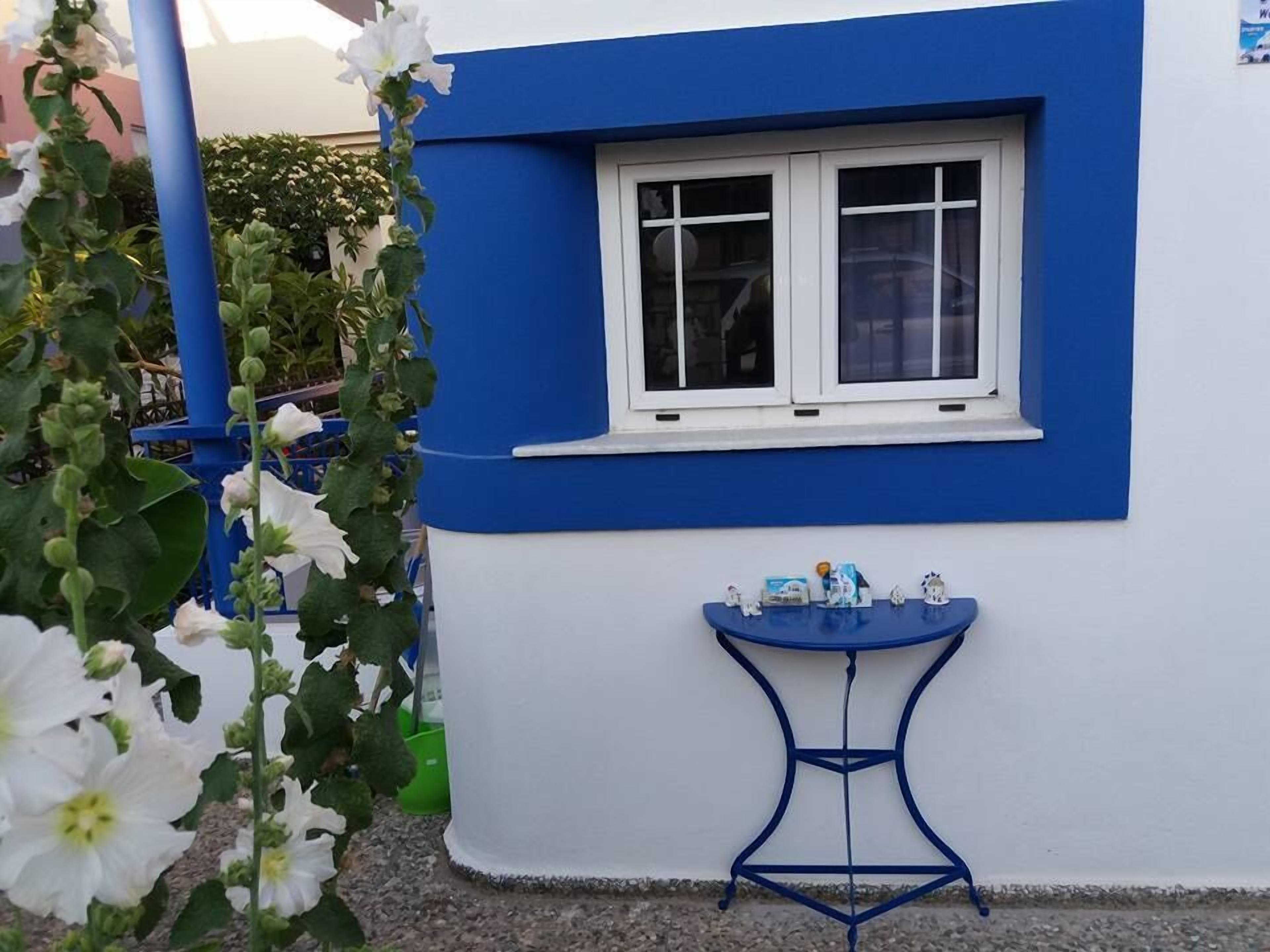 Un edificio con fachada azul y blanca, una ventana y una pequeña mesa azul con objetos encima.