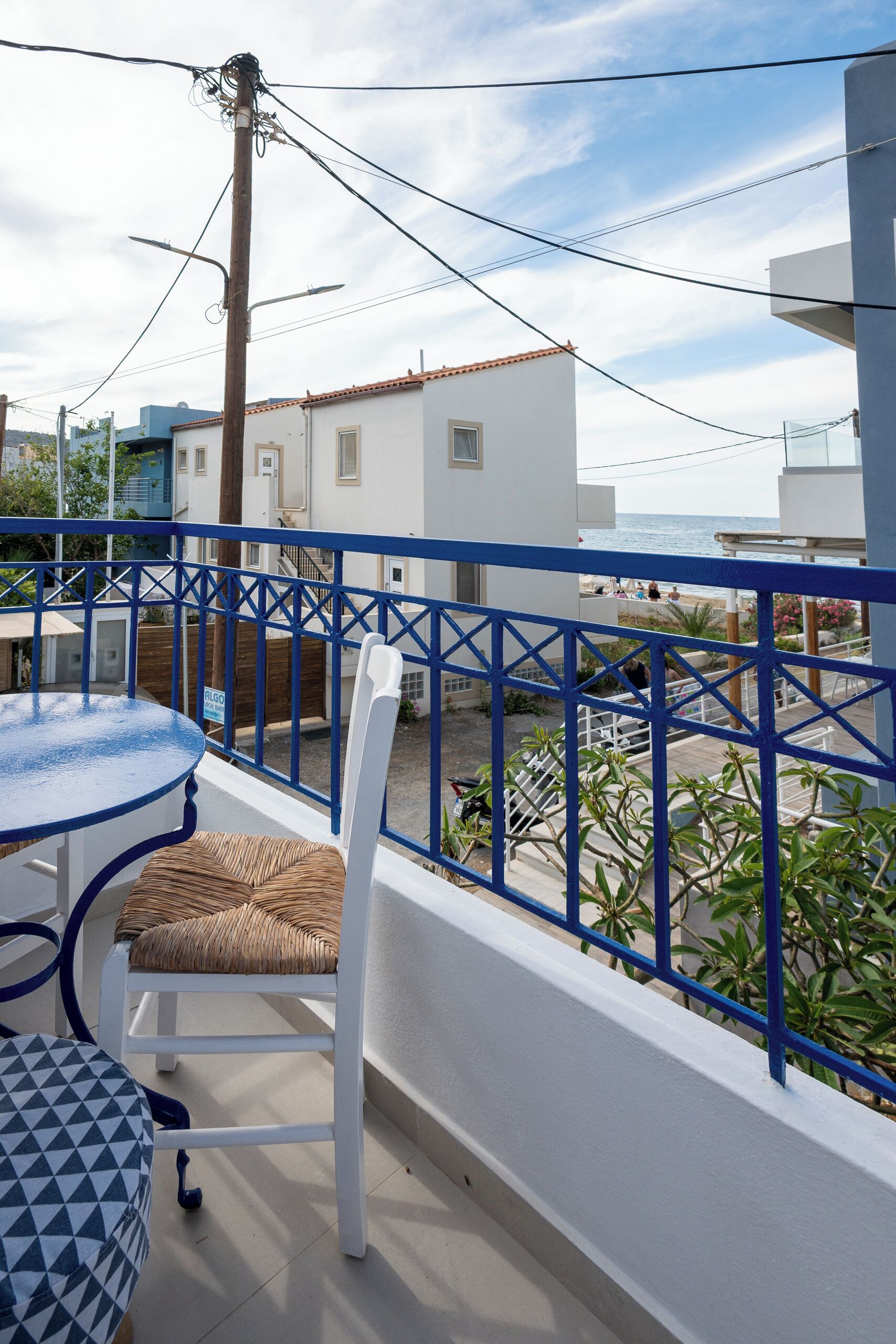 Ein Balkon mit Tisch und Stuhl, Blick aufs Meer und ein Gebäude im Hintergrund.