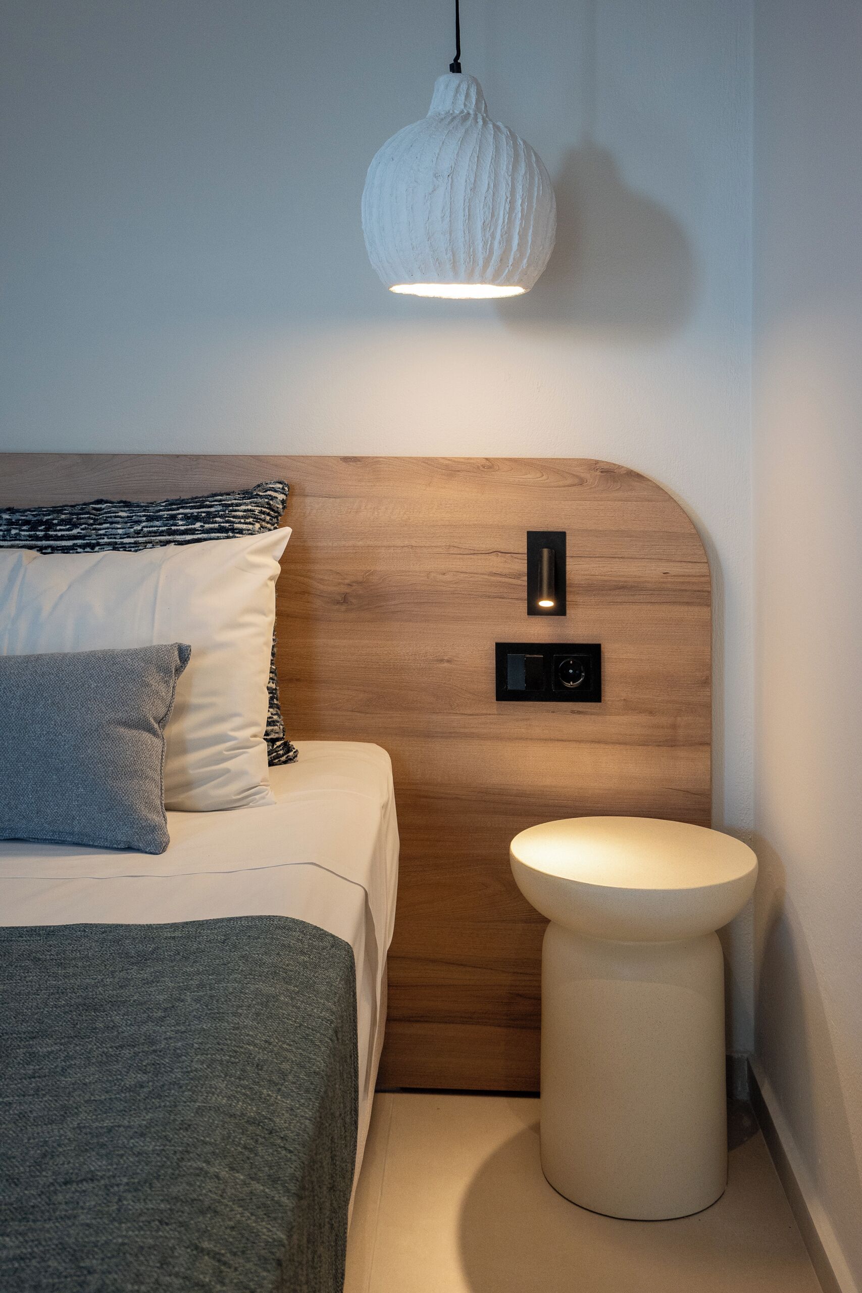 Un dormitorio moderno con cabecera de madera, una mesita de noche, una lámpara colgante e interruptor en la pared.