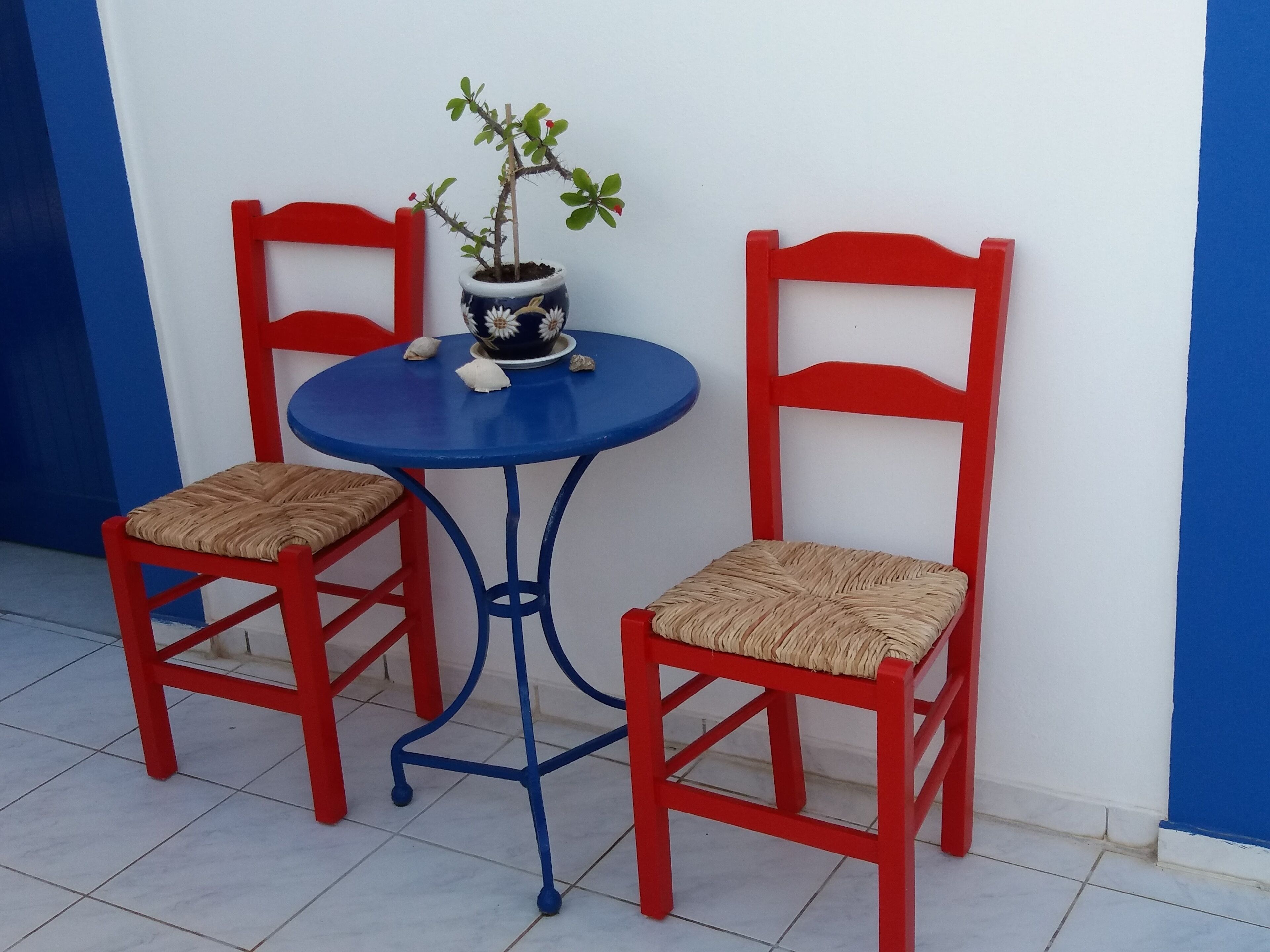 Zwei rote Stühle mit geflochtenen Sitzflächen und ein kleiner blauer Tisch mit einem Blumentopf.
