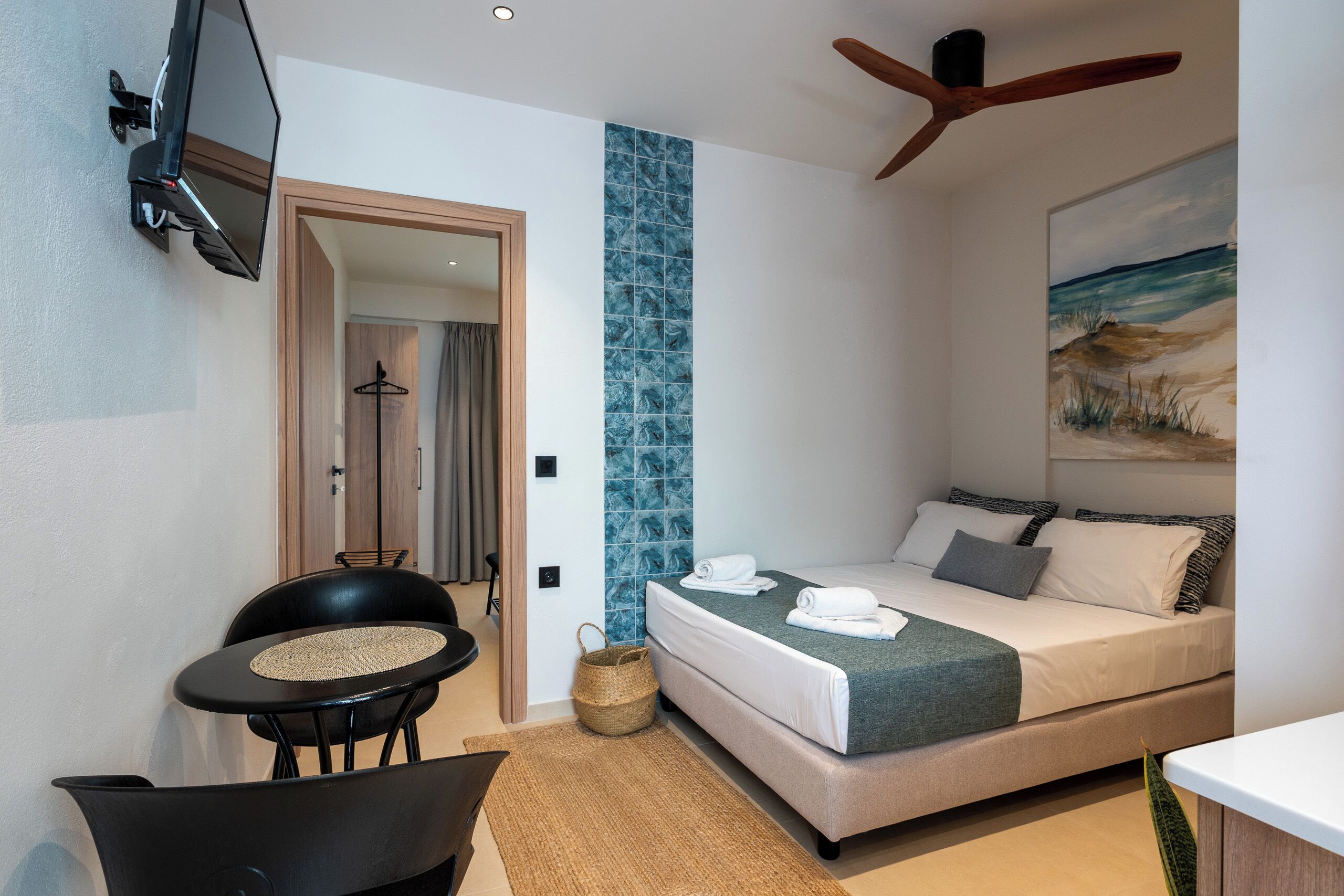 A bedroom with a bed, a desk, a chair, a TV, and a ceiling fan.
