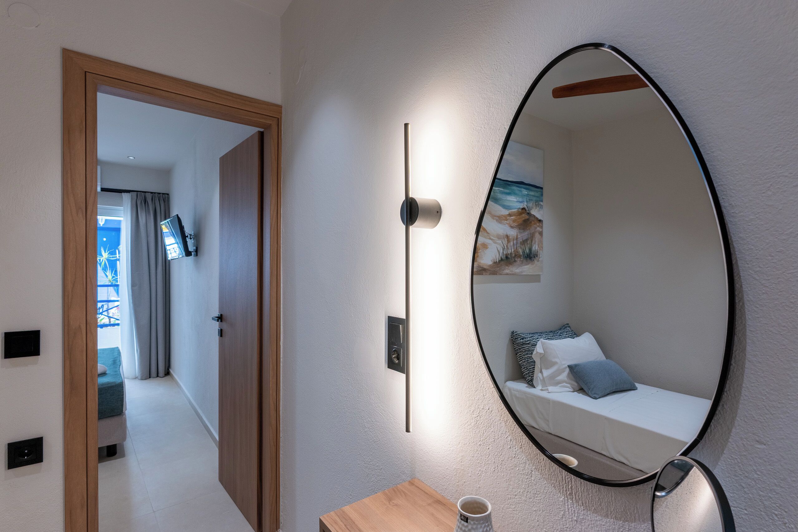 Een moderne kamer met een bed, een ronde spiegel, een nachtkastje met een kopje, en een deur naar een andere kamer.