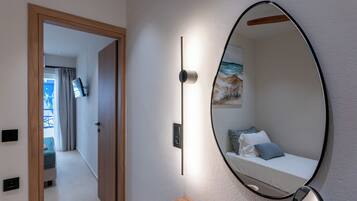 Een moderne kamer met een bed, een ronde spiegel, een nachtkastje met een kopje, en een deur naar een andere kamer.