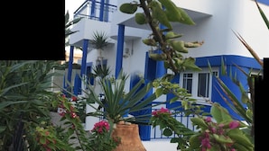 Ein Gebäude mit blauen und weißen Außenwänden, einem Balkon und einer großen Vase mit Grünpflanzen und rosa Blumen.