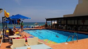 Ein Poolbereich mit Liegestühlen und Sonnenschirmen sowie Blick auf das Meer.