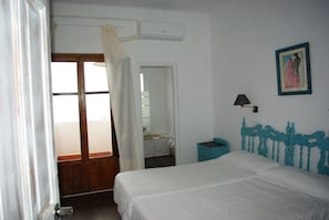 A bedroom with a bed, a nightstand, a wall-mounted lamp, a painting, and a bathroom visible through an open door. - Hotel Lanjarón (Lanjaron)