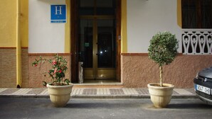 A hotel entrance with a green awning, a blue sign with an 'H' and 'CIUDAD', and two potted plants on the sidewalk. - Hotel Lanjarón (Lanjaron)