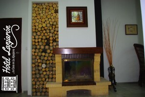 A fireplace with a log wall behind it, a framed picture above the fireplace, and a sign on the left. - Hotel Lanjarón (Lanjaron)