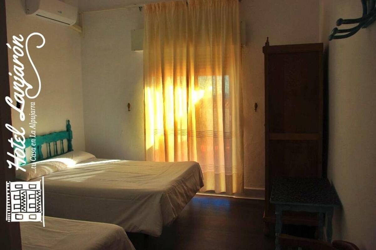 A hotel room with two beds, a wooden wardrobe, and a small table.