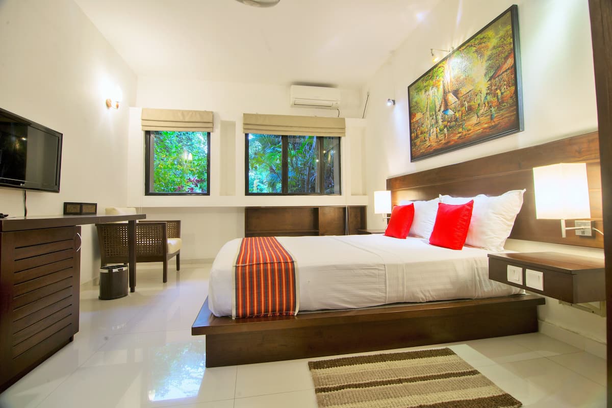A modern hotel room with a large bed, a desk, a television, and a painting on the wall.