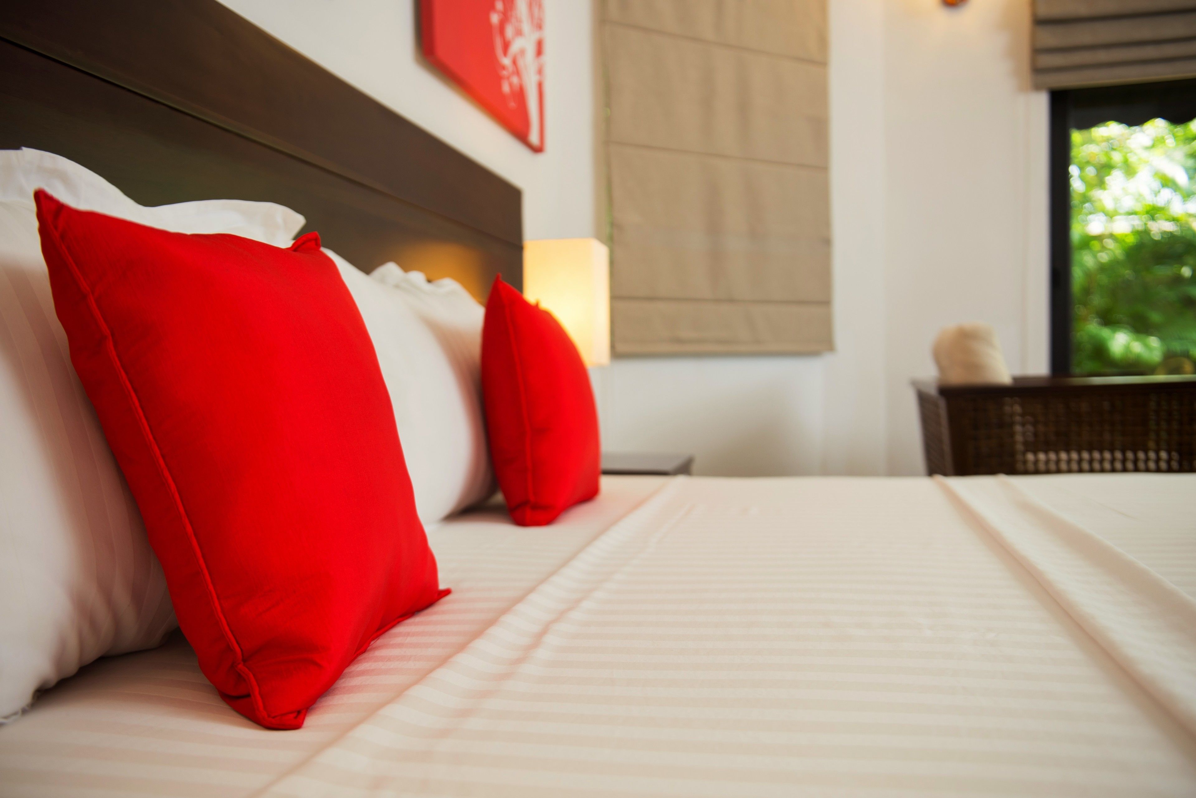 A neatly made bed with red and white pillows, a headboard, and a bedside table with a lamp.