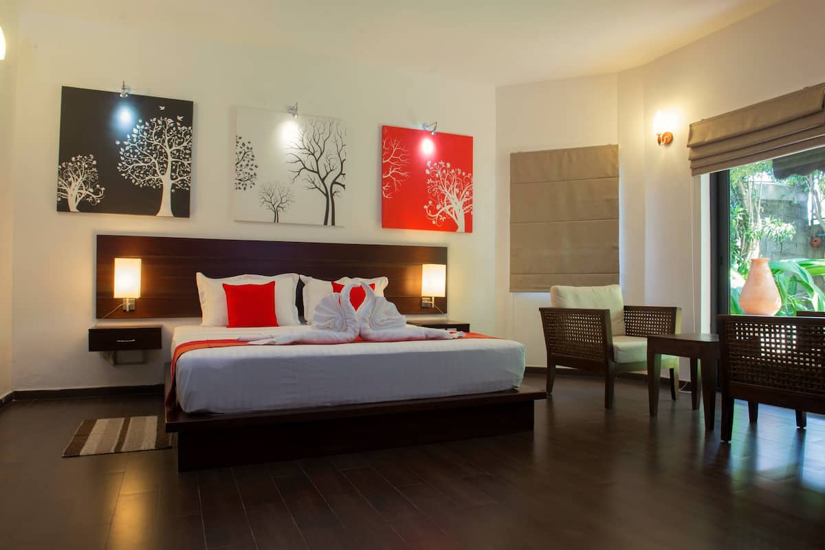 A hotel room with a large bed, two bedside tables, a nightstand, a seating area with chairs, and artwork on the walls.