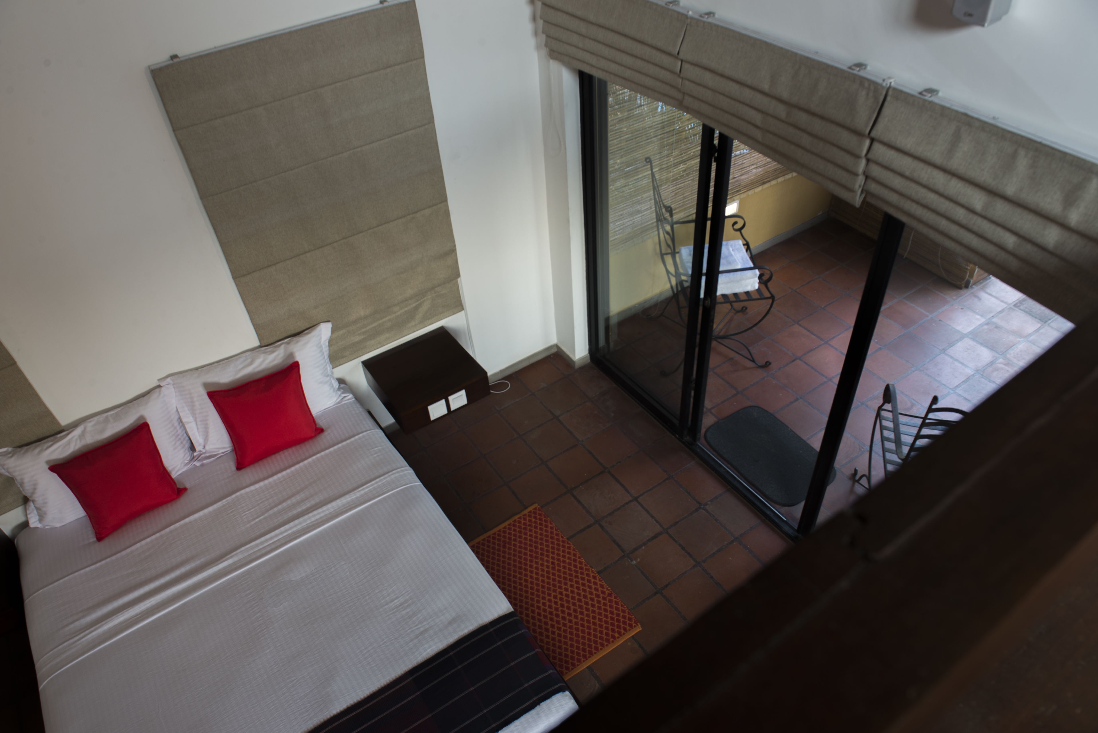 Une chambre d’hôtel avec un lit, une fenêtre avec des stores et une vue sur un espace extérieur aménagé avec une table et des chaises.
