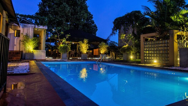 A swimming pool with a clear view of the surrounding area, including a building with a glass facade and a covered seating area. - Villa Escondite (Sri Jayawardenepura Kotte)