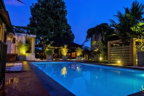 A swimming pool with a clear view of the surrounding area, including a building with a glass facade and a covered seating area. - Villa Escondite (Sri Jayawardenepura Kotte)
