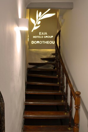 A staircase with a wooden handrail and a sign for Enea Hotels Group in the background. - Elia Dorotheou (Chania)