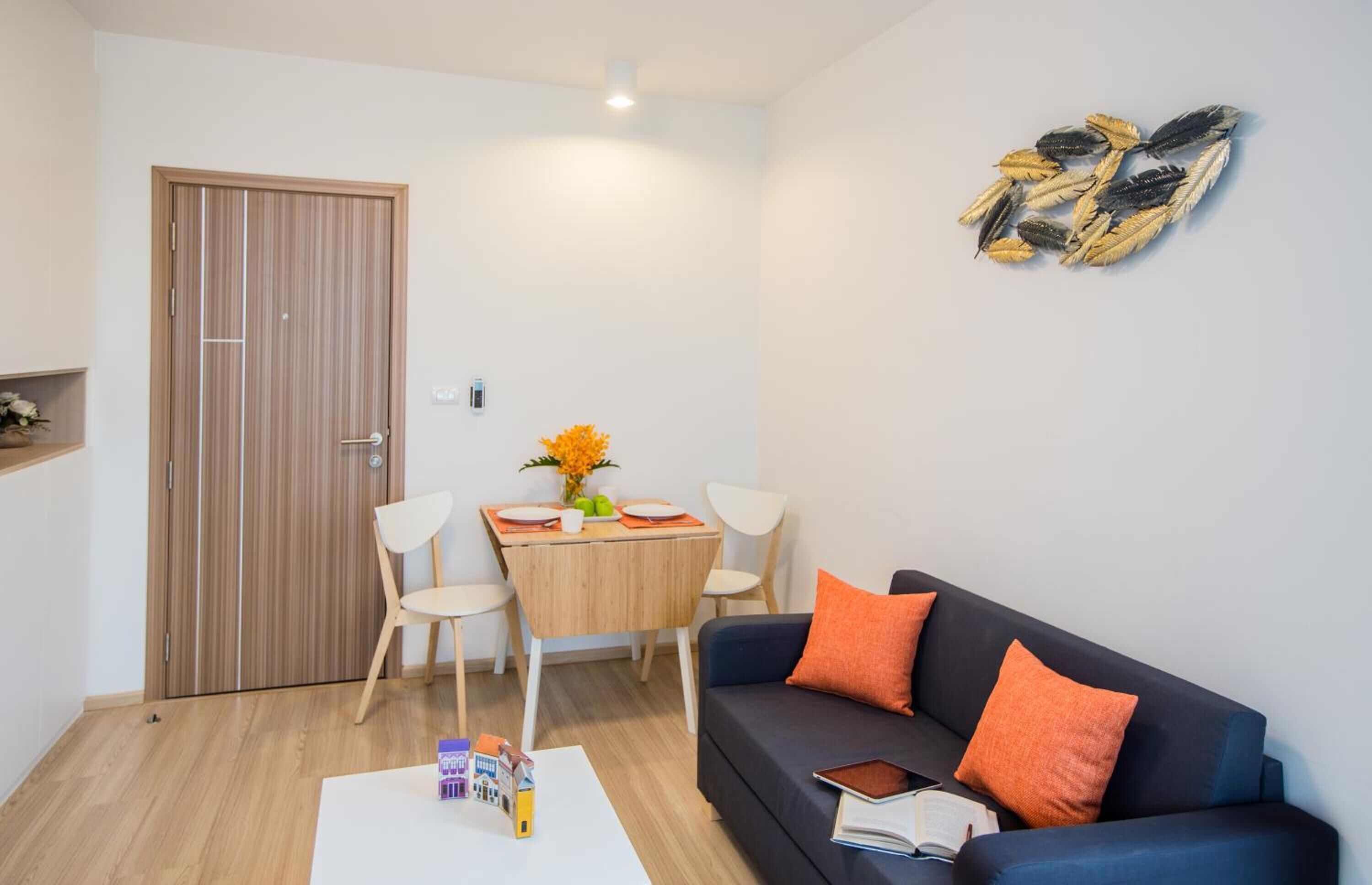 A compact living space with a dining area, a sofa with orange cushions, and a decorative wall piece.