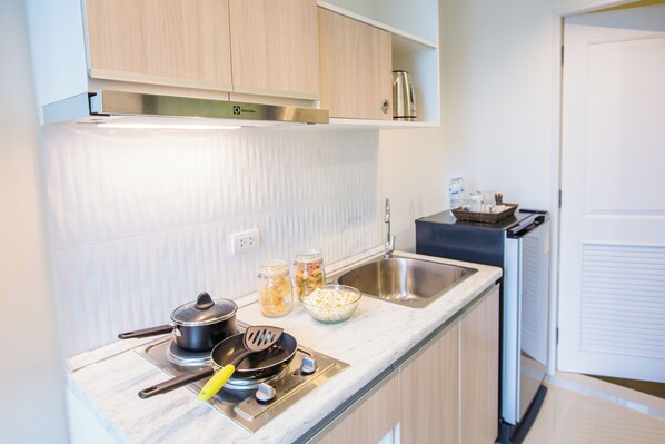 A modern kitchen with a built-in stove, a sink, and a countertop with jars of pasta and a bowl of cereal. - Connext Residence Phuket (Phuket)